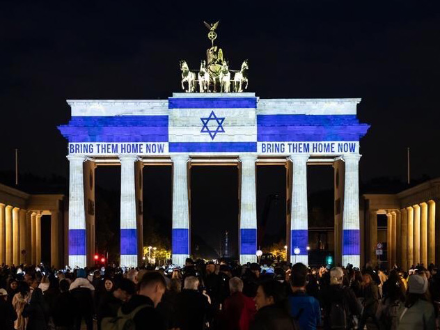 The picture for the study of German-Israeli cultural relations shows the Brandenburg Gate at night with a projection of the Israeli flag and the text “BRING THEM HOME NOW”, surrounded by a crowd of people.