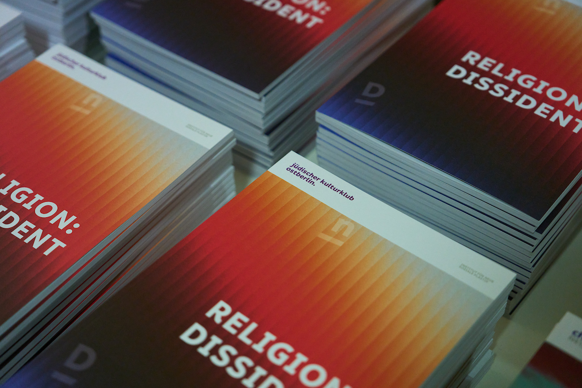The picture shows several stacks of the publication »Religion: Dissident« published by the Institute. The cover has a color gradient illustrated by colorful stripes.